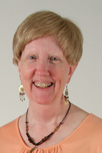 Francie Cuffney smiling at the camera with gold earrings and an orange shirt.