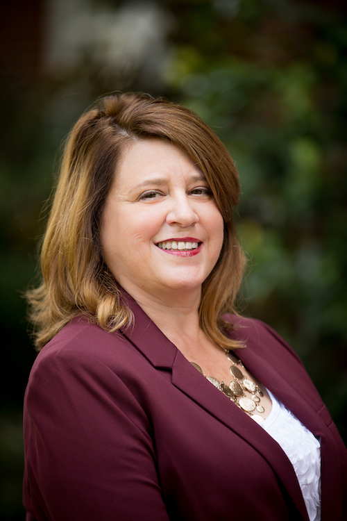 Liz Wolfinger smiling at the camera in a white blouse with a maroon blazer.